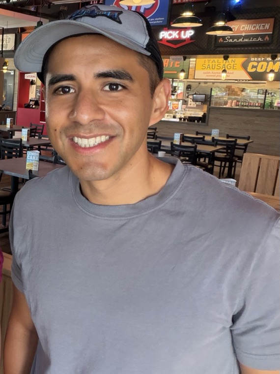 Portrait of Daniel Deleon smiling, wearing a baseball cap